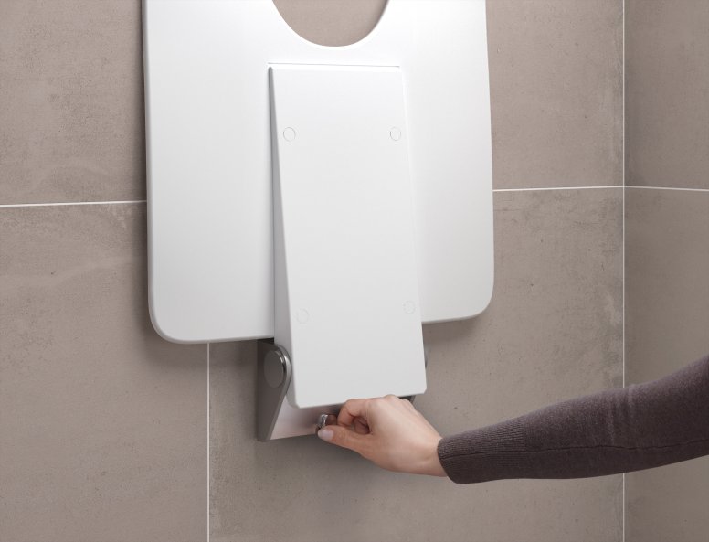 Beige tiled wall with a removable white shower seat that is mounted by one hand